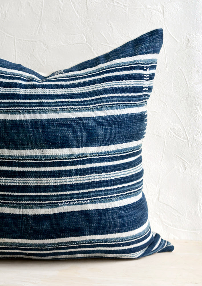 A throw pillow made from dark indigo fabric with white stripes and embroidery detailing.