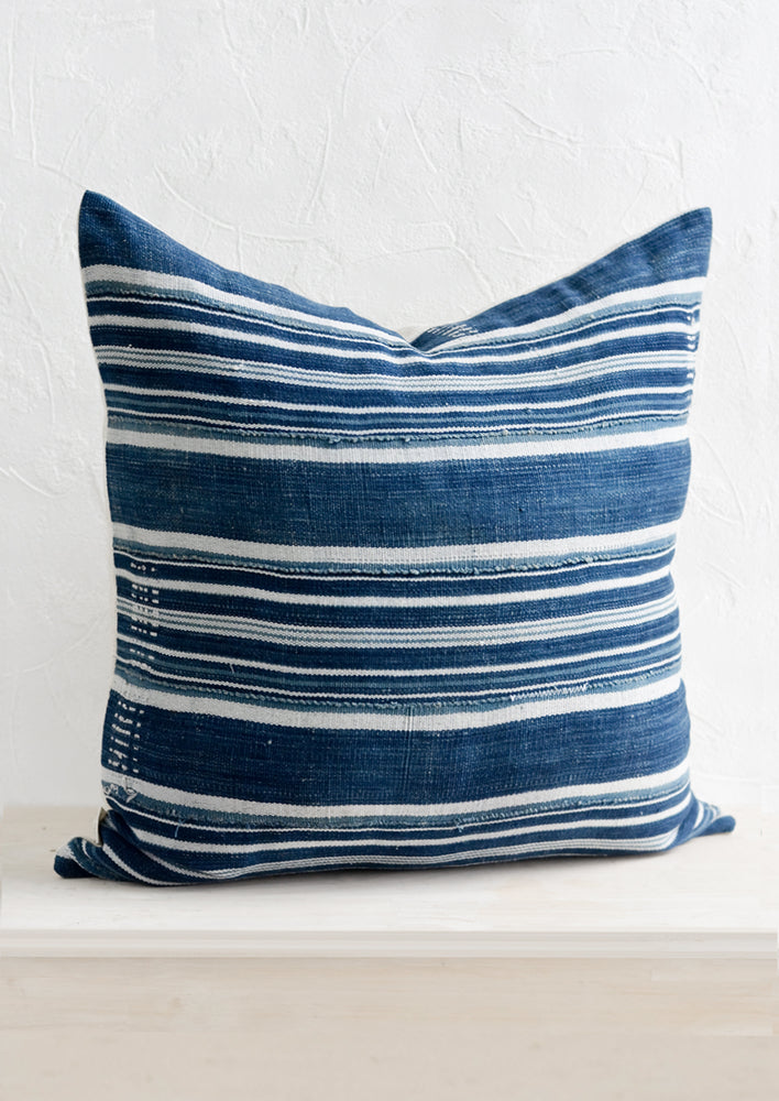 A throw pillow made from dark indigo fabric with white stripes and embroidery detailing, on a bench.
