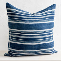 2: A throw pillow made from dark indigo fabric with white stripes and embroidery detailing, on a bench.