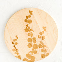 1: A round maple wood cutting board with laser etched eucalyptus print.