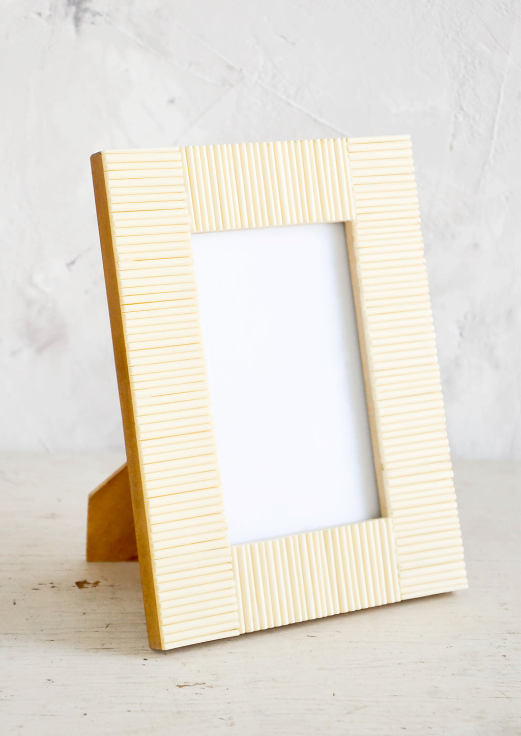 1: Empty picture frame on table. Frame is cream colored with ribbed texture made from bone.