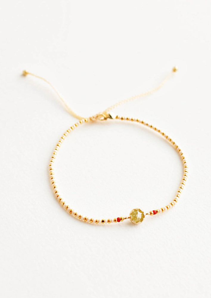 Delicate bracelet of white and gold beads and a yellow crystal charm flanked by two red beads. 