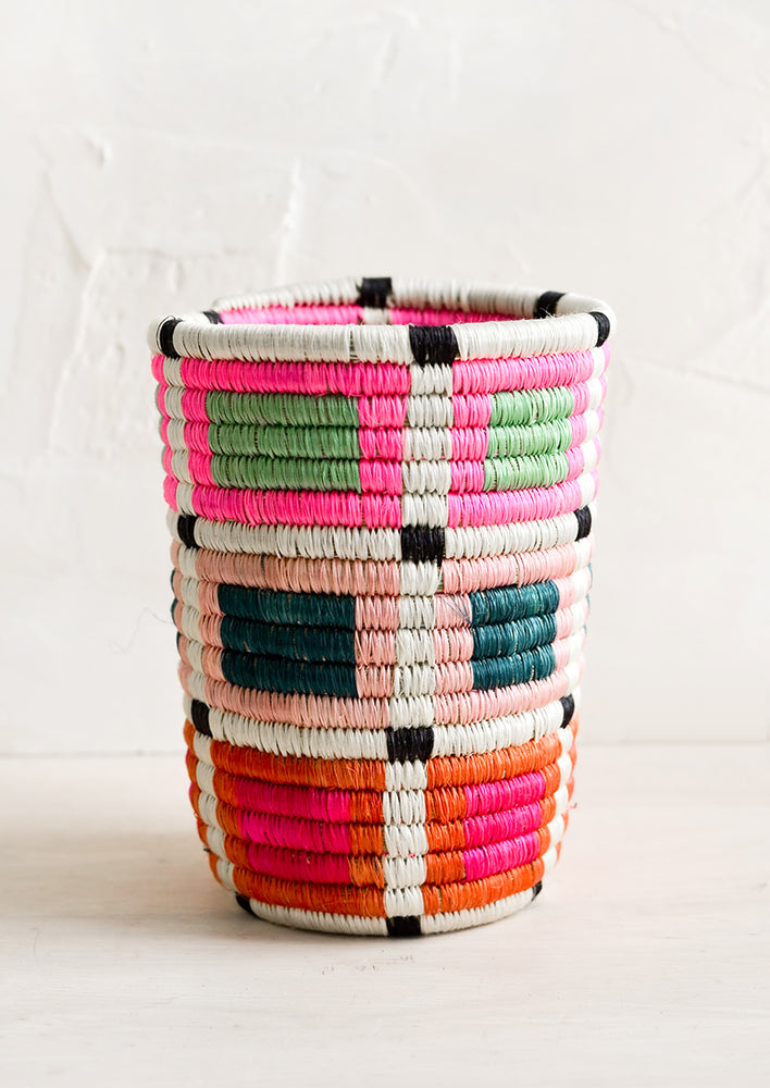 Pencil cup shaped basket woven from multicolor sweetgrass. Mix of bright colors in a geometric pattern.