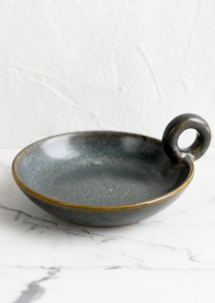 A round ceramic dish in blue glaze with handle.