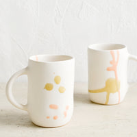 2: Two white ceramic mugs with hand painted peach and mustard glaze drips.