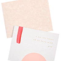 2: A pale tan envelope and white greeting card with a rectangle of red paint, a semicircle of pink paint, and gold foil text reading "I'm all sorts of in love with you."