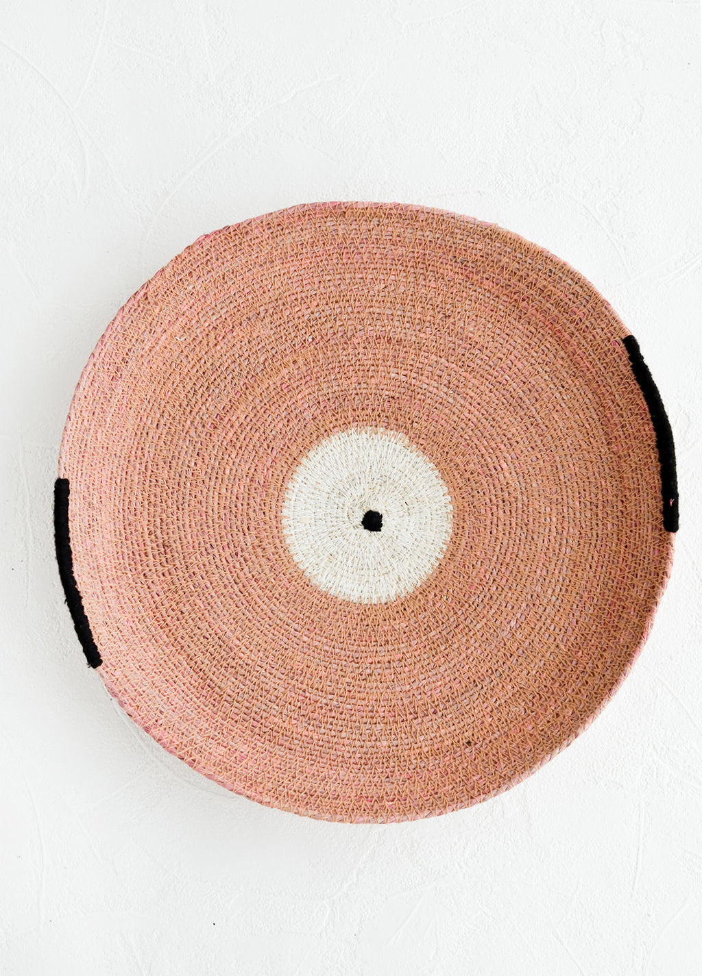 Rose: A round platter/tray made from woven seagrass in pink, white and black.