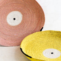 3: Two round platters/trays made from woven seagrass in yellow and pink.