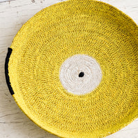 Yellow: A round platter/tray made from woven seagrass in yellow, white and black.