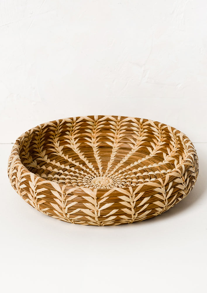 A shallow, round basket with lighter woven pattern throughout.