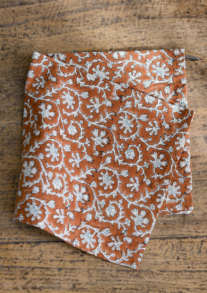 A square cotton dinner napkin in amber and white floral print.