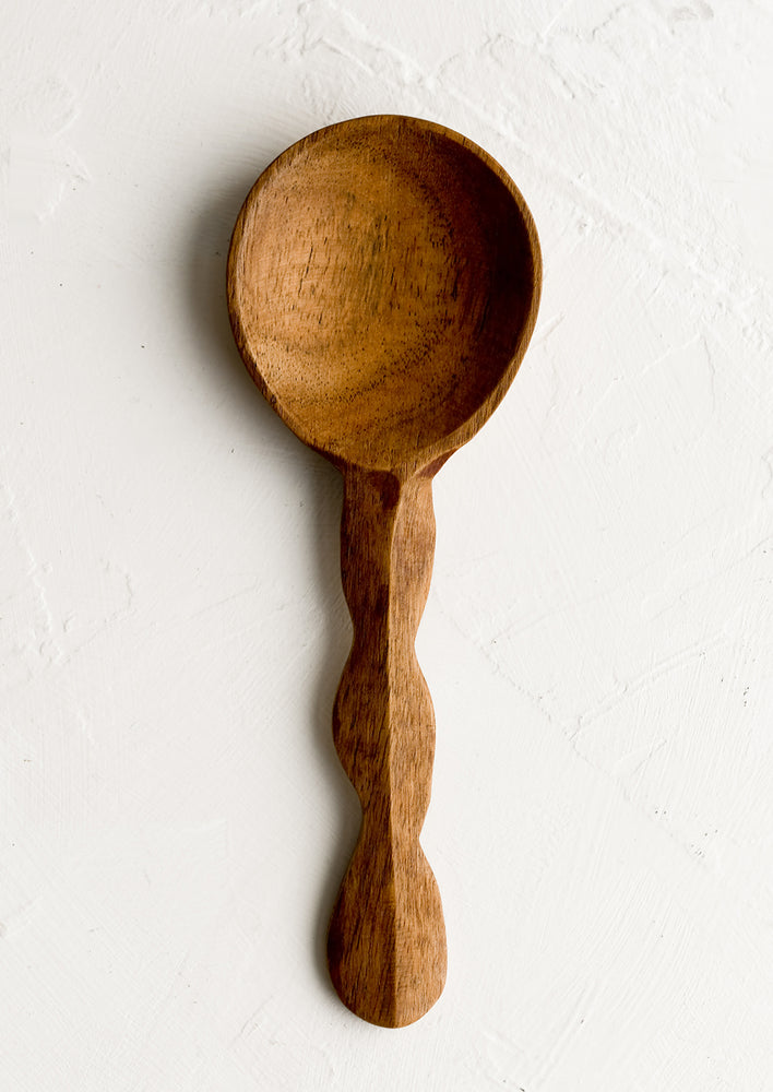 A brown wooden spoon with decorative curvy handle.