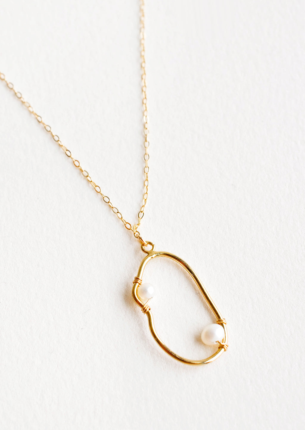 1: Gold necklace with asymmetric round gold charm made from a slim gold hoop, with two pearls attached with wrapped wire.