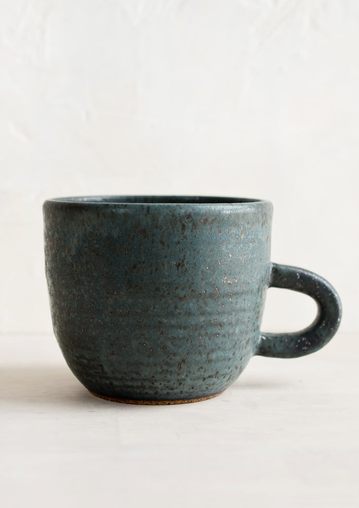 A short ceramic coffee mug in matte dark blue glaze with black speckles.