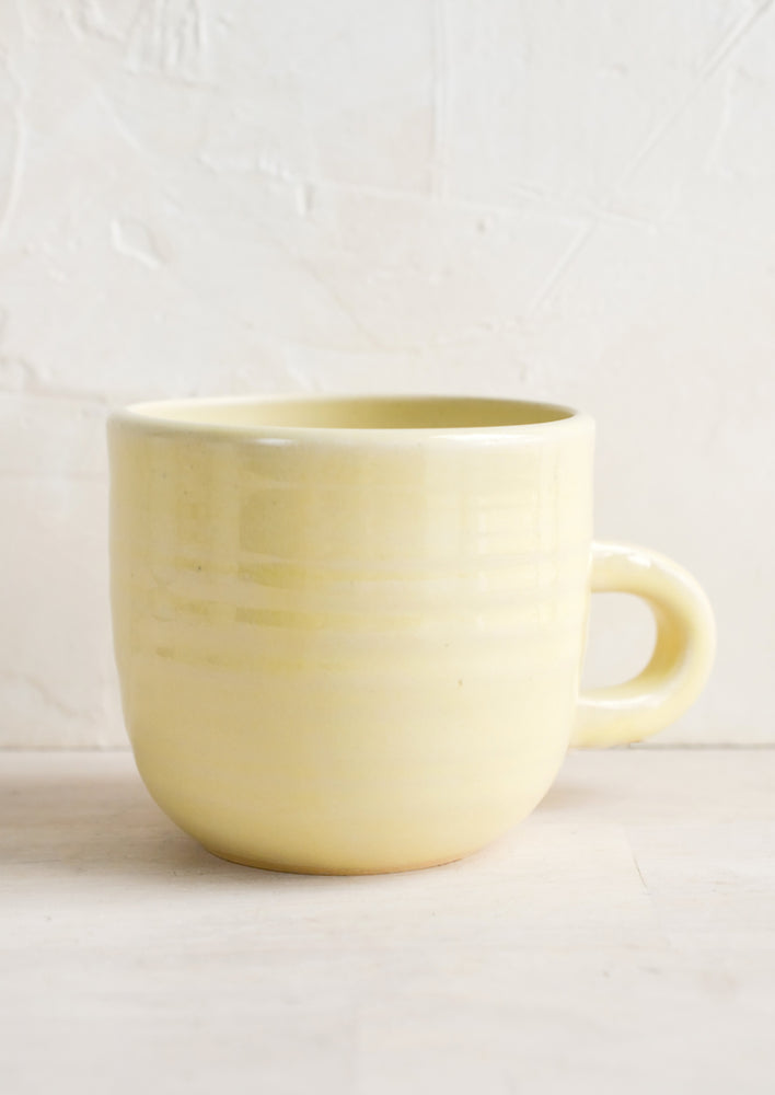 A short ceramic coffee mug in glossy pale yellow glaze.