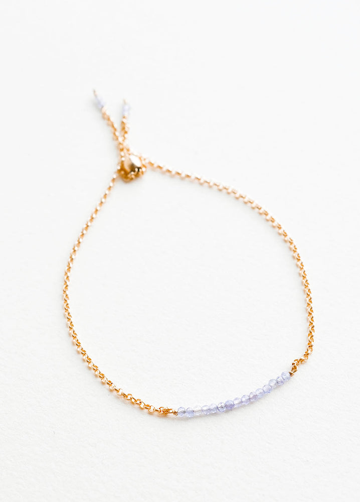 A delicate gold chain bracelet featuring a row of miniature light blue gemstones.