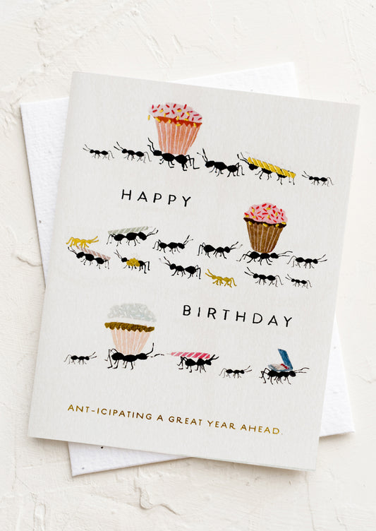 A card with illustration of ants carrying around cupcakes and birthday candles, text reads "Ant-icipating a great year ahead".