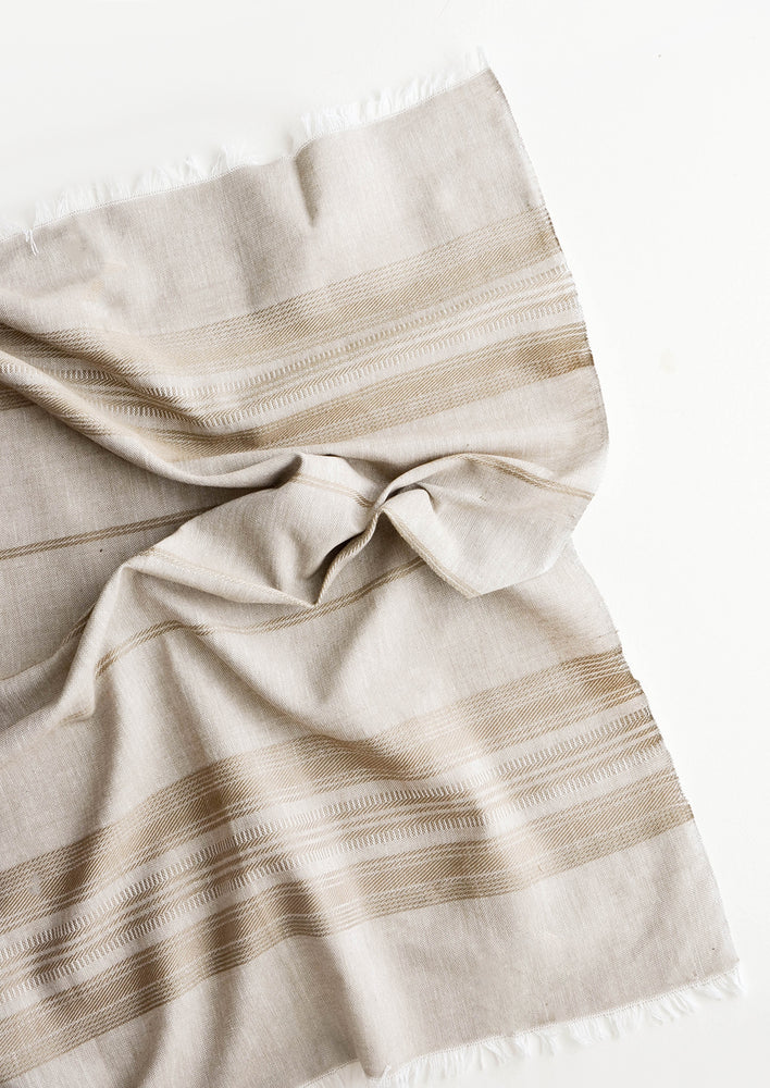 A crumpled brown cotton towel with textured stripe and fringe edge.