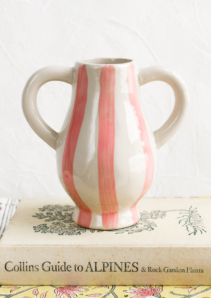 A ceramic vase in pink stripe pattern with side handle detail.