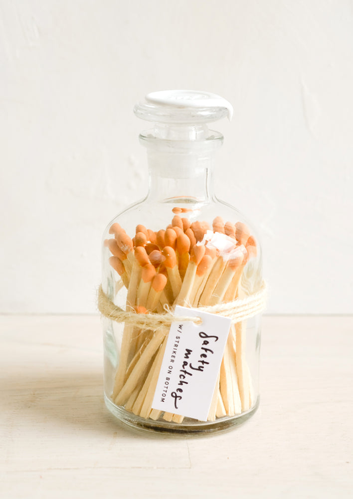 Safety matches with orange tips in a vintage-style glass apothecary jar with white wax seal on lid.