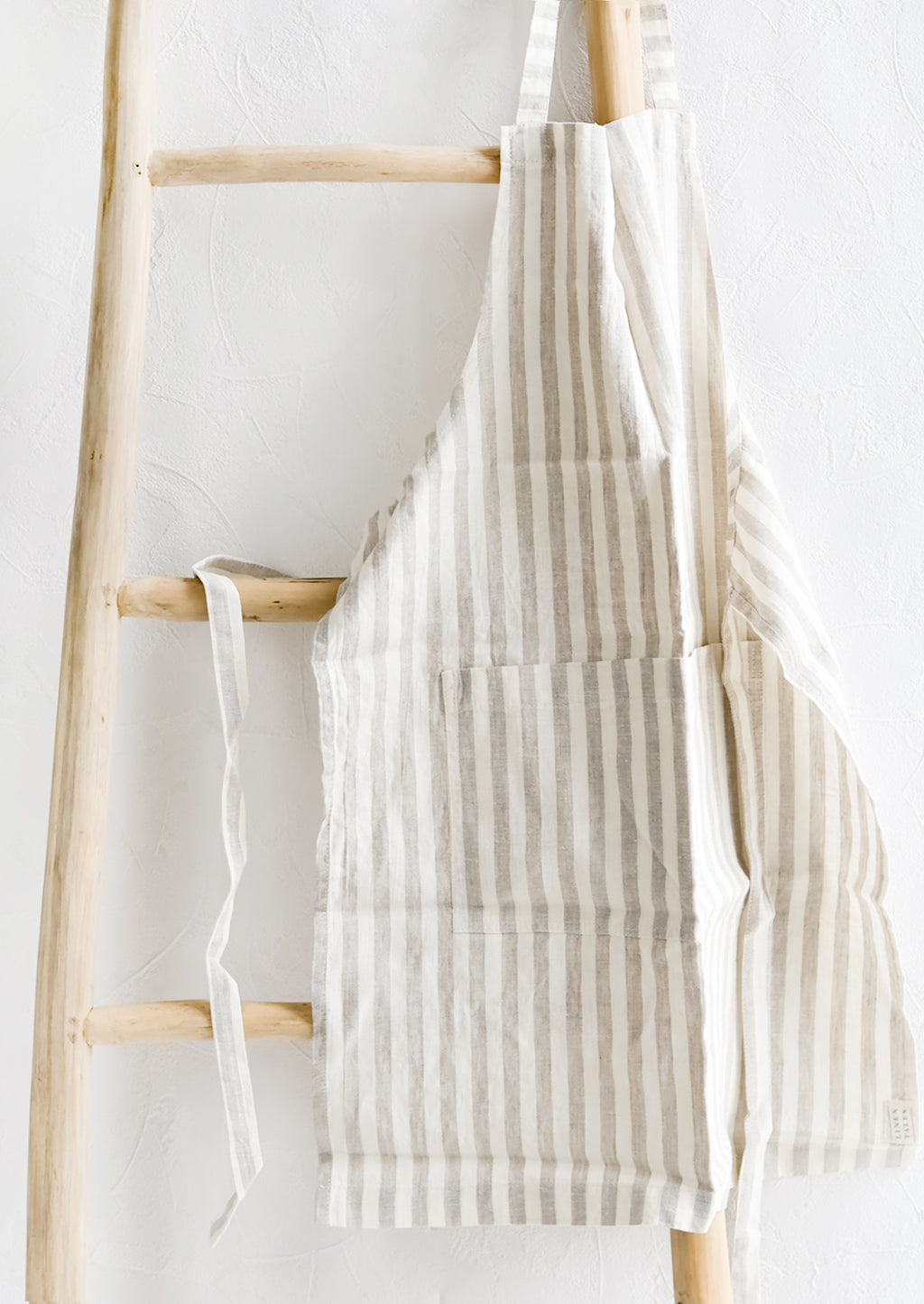 Natural Stripe: A tan and white striped linen apron hung on a wooden ladder.