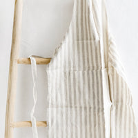 Natural Stripe: A tan and white striped linen apron hung on a wooden ladder.