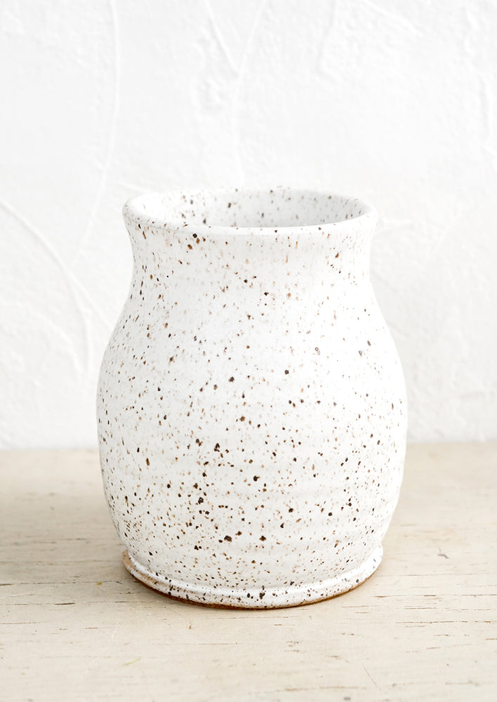 A curvy ceramic vase in matte white glaze with brown speckles.