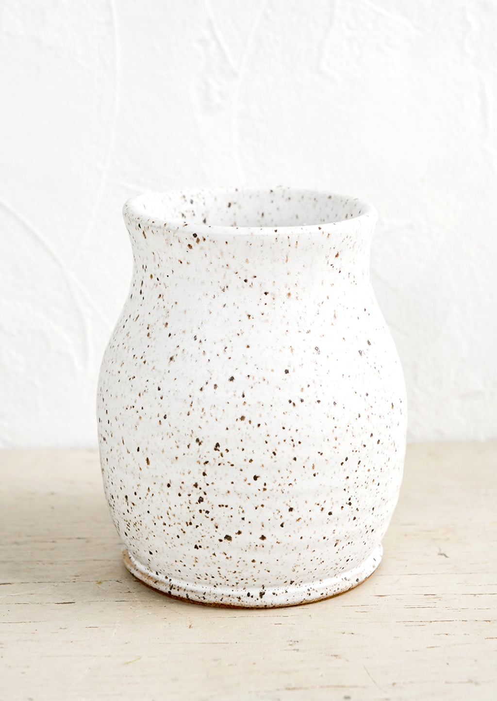 1: A curvy ceramic vase in matte white glaze with brown speckles.