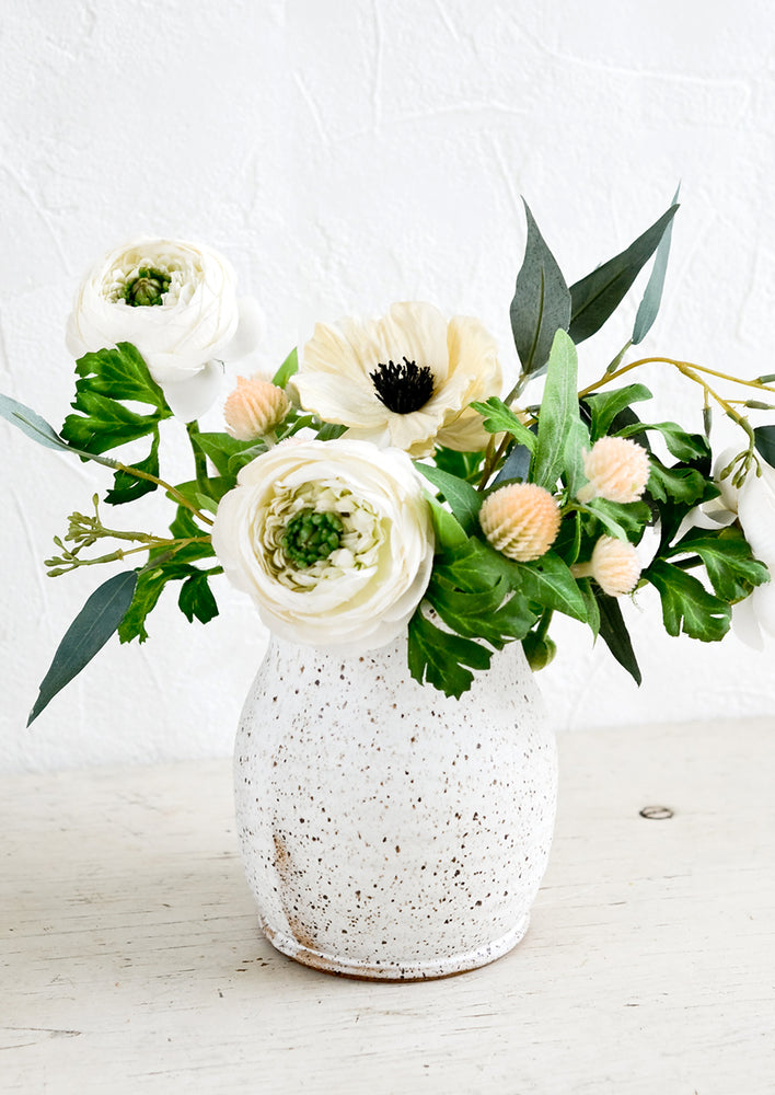 2: A speckled ceramic vase with a floral arrangement of white anemone and ranculus.
