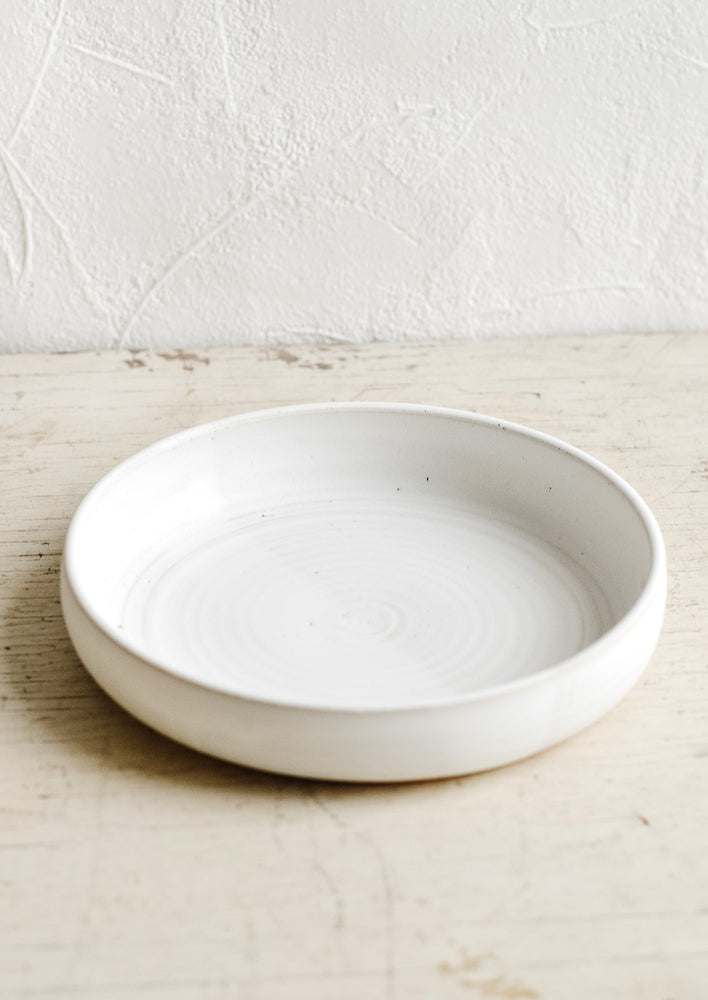 A shallow and wide ceramic bowl in a matte white glaze.