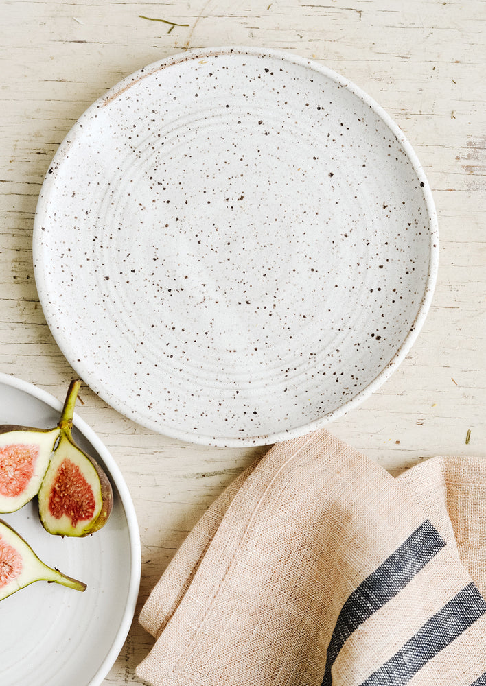 A ceramic side plate in matte white with dark speckles.