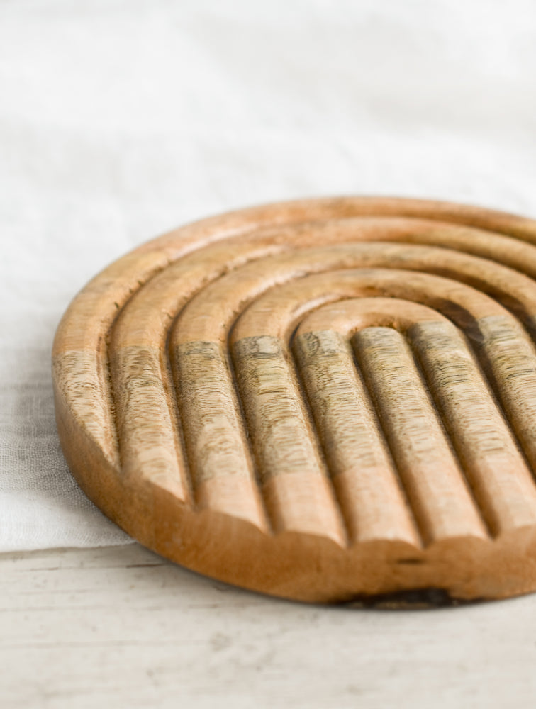 2: A round wooden trivet with inset arch pattern.