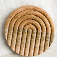 1: A round wooden trivet with inset arch pattern.