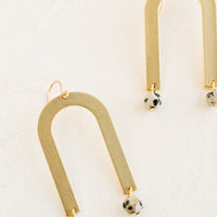 Dalmatian Jasper: A pair of drop earrings with archway shape made of brass and speckled gemstone beads at bottom.
