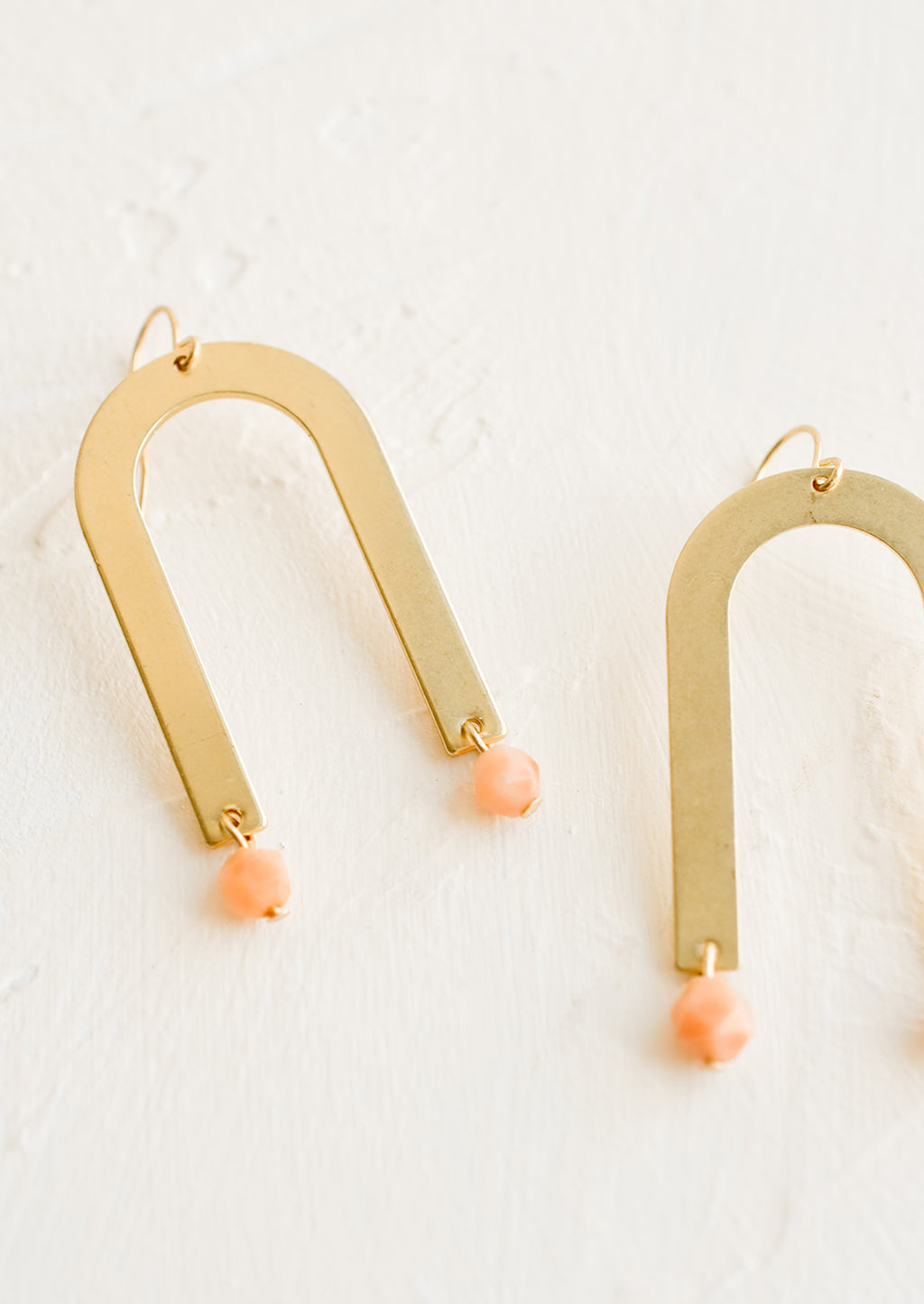 Sunstone: A pair of drop earrings with archway shape made of brass and pink gemstone beads at bottom.