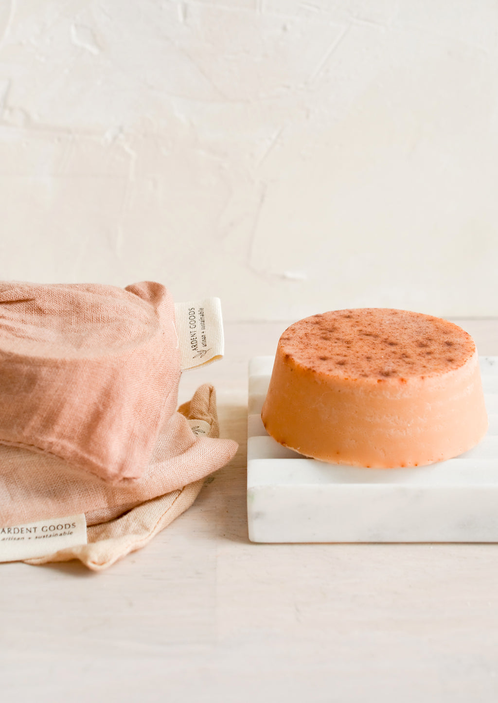 3: A round soap bar with naturally dyed muslin pouches on marble soap dish.