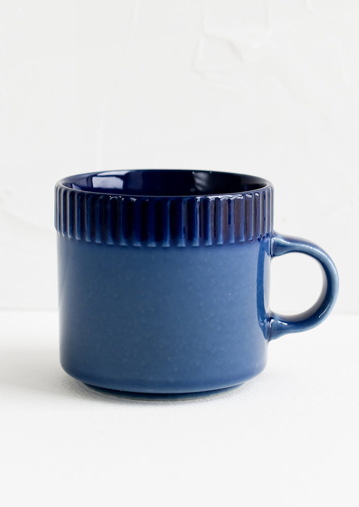 A ceramic mug in cobalt blue with ribbed tonal border along rim.