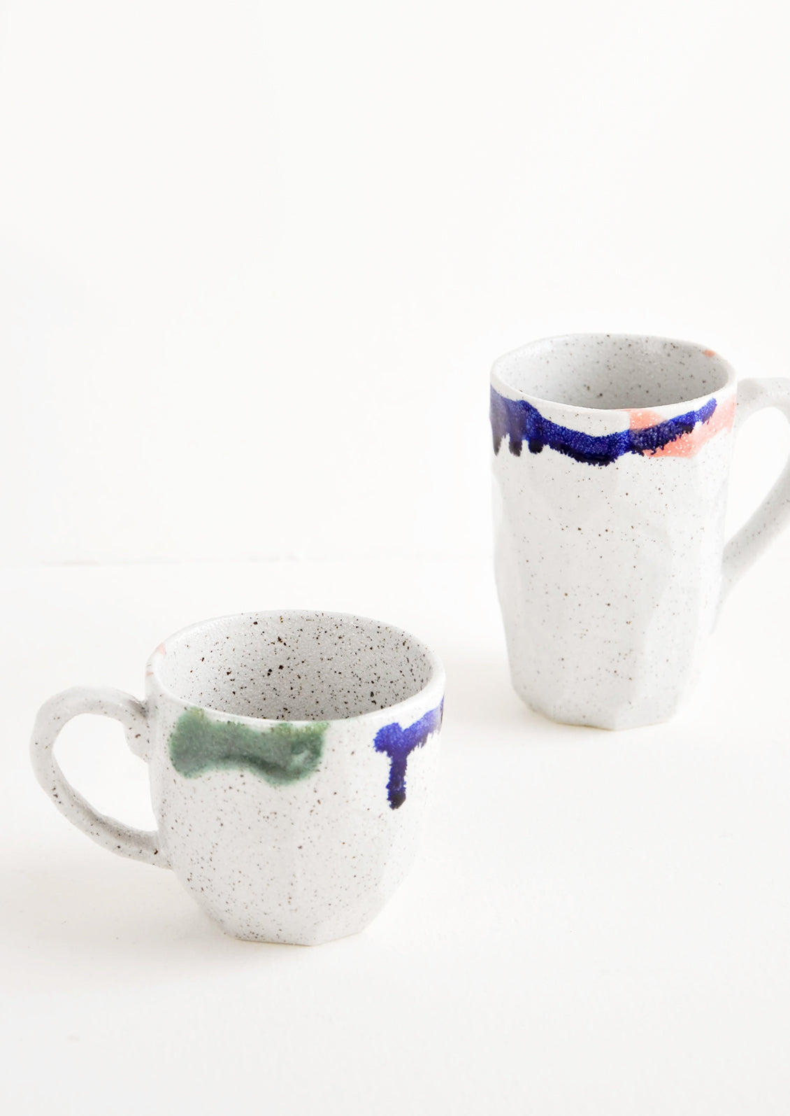 Two differently sized gray ceramic mugs with blue, green, and pink painted rims.