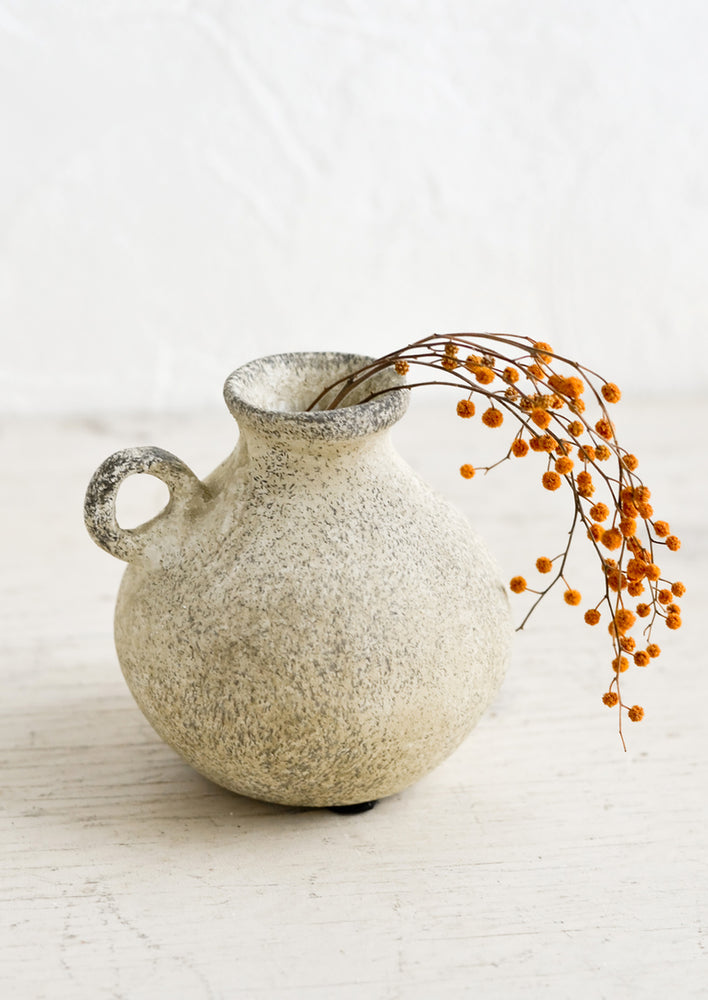 A petite ceramic bud vase in tan patina finish, holding dried mimosa sprig.