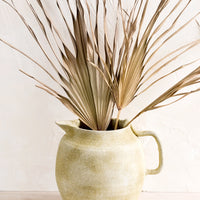 2: A ceramic pitcher meant to be used as a vase in distressed clay with dried palm leaf.