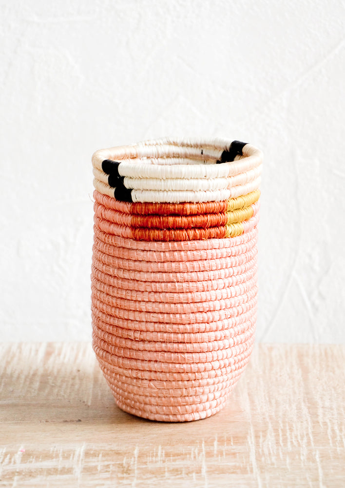 Pencil cup shaped woven sweetgrass basket in pink color combo with geometric trim, sitting on a table.