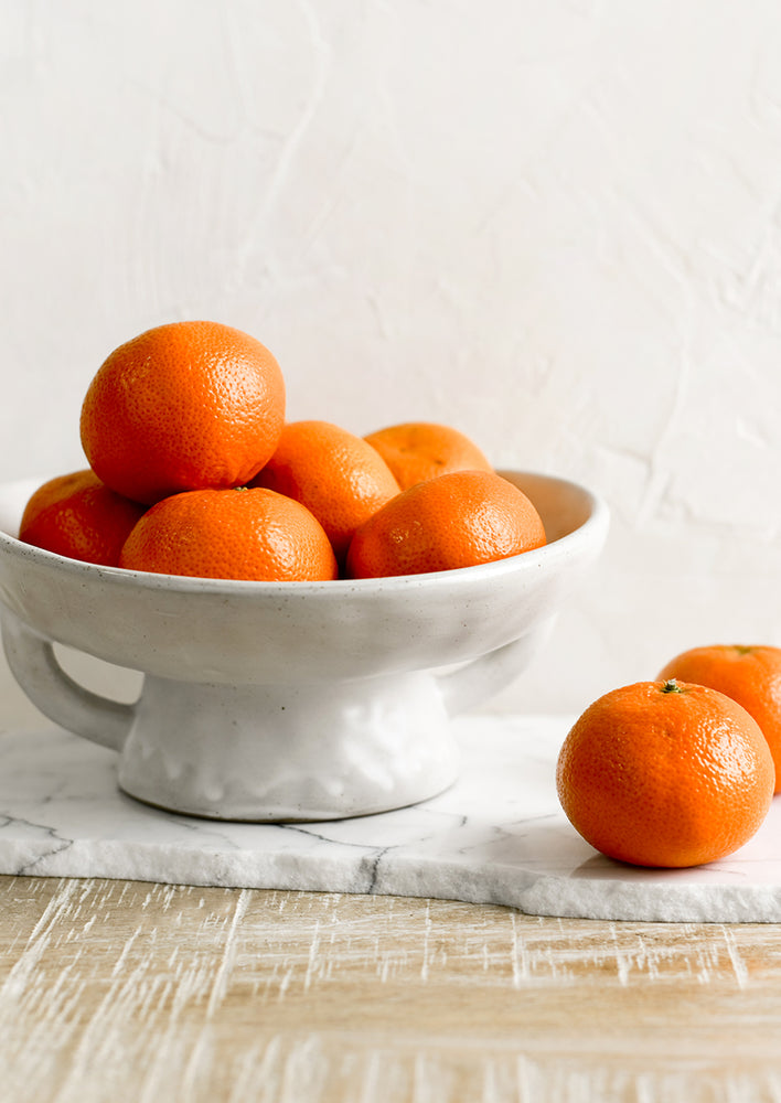 1: A footed ceramic bowl holding oranges.
