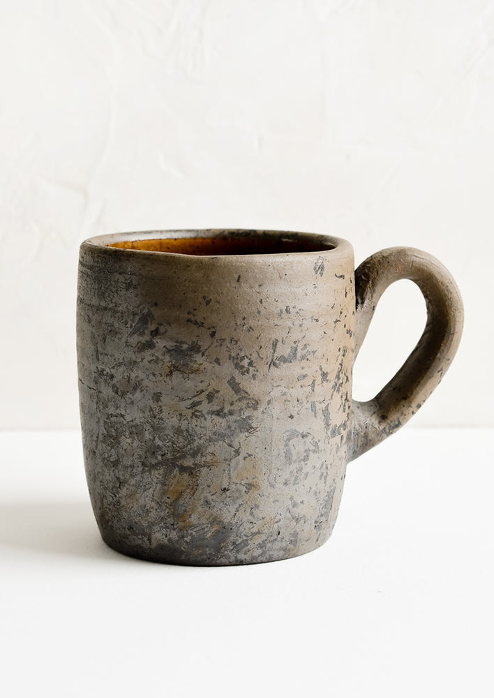 A coffee mug made from raw, unglazed dark brown clay.