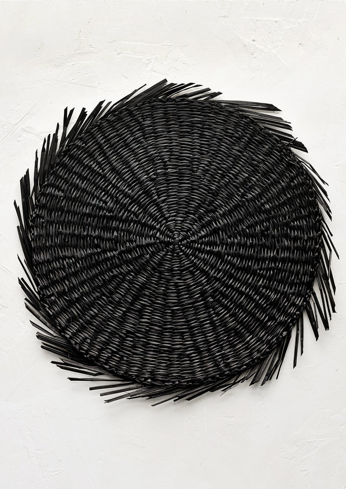 Black: A round straw placemat in black with curvy fringe trim.