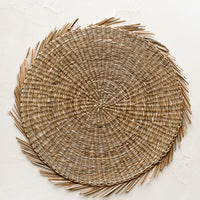 Natural: A round straw placemat in natural with curvy fringe trim.