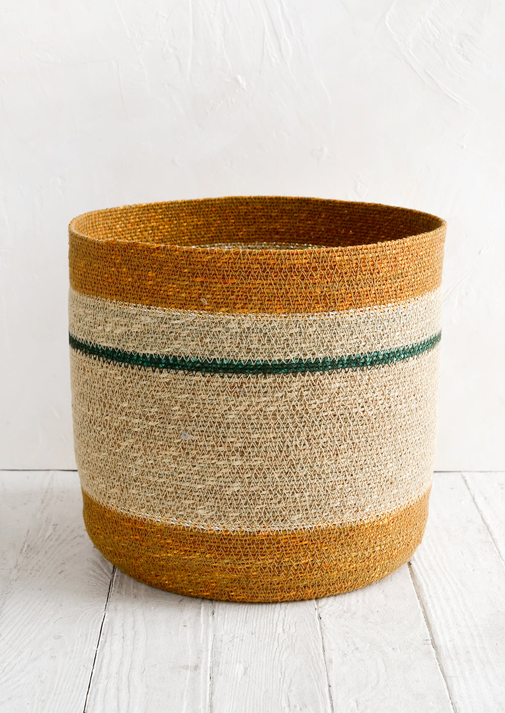 1: A round open-top storage basket woven from seagrass in ochre, natural and teal stripes.