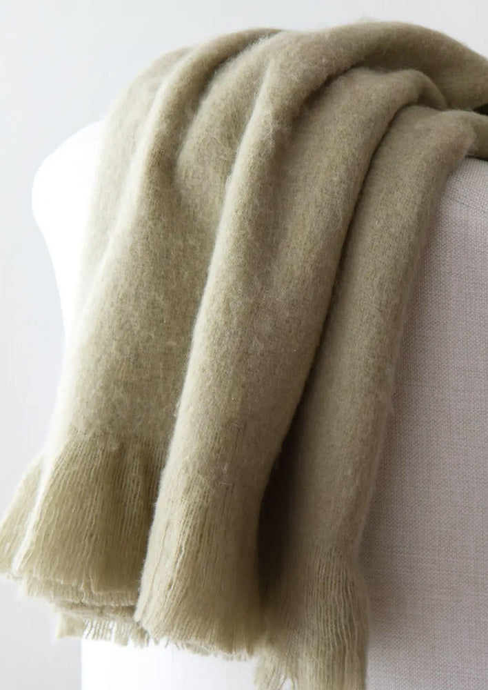 A sage green mohair throw blanket draped over a chair.
