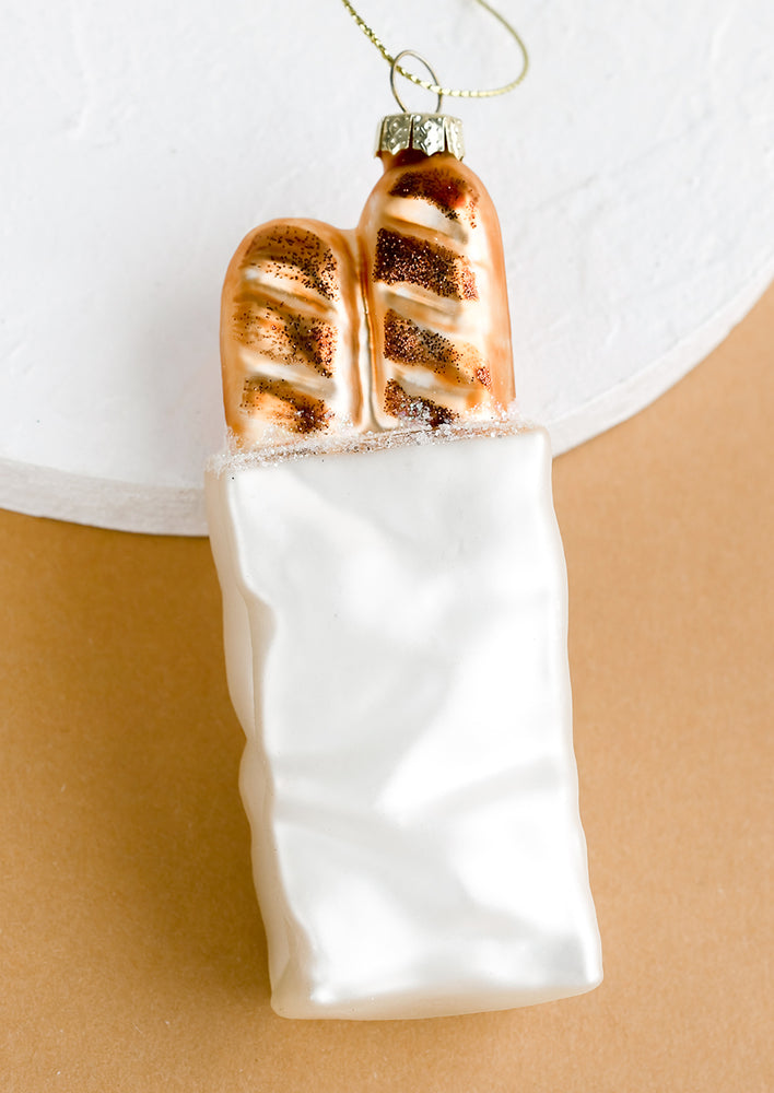 1: An all glass holiday ornament of a white paper bag with two baguettes poking out of the top.