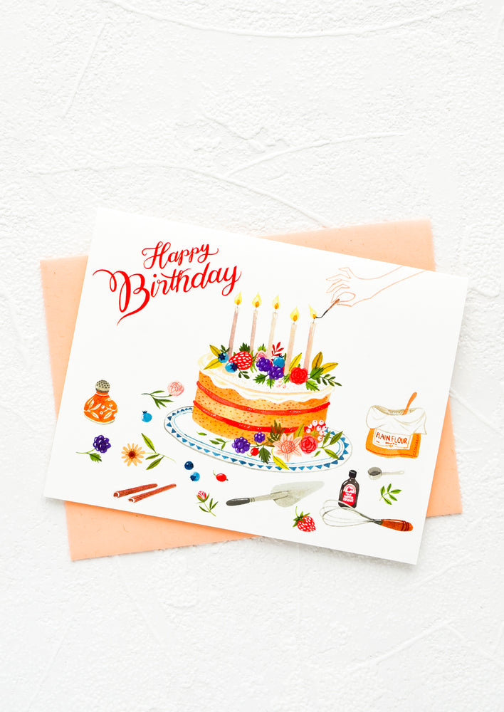 Greeting card with cake surrounded by baking equipment, "Happy Birthday" script in red letters.