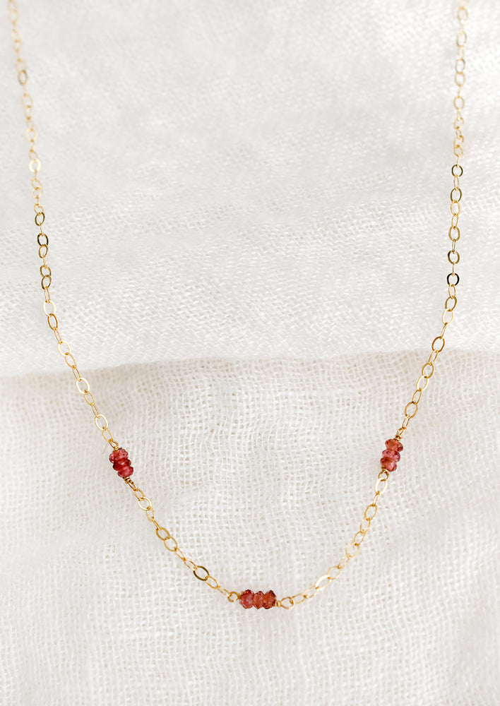 A delicate gold chain necklace with garnet beaded stations.